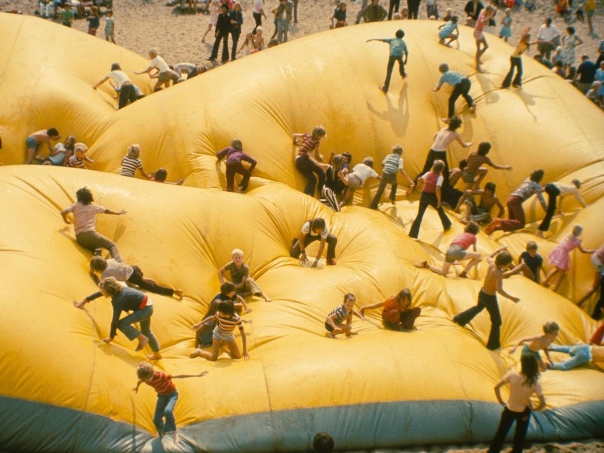 People climb and run across a large yellow inflatable landscape.